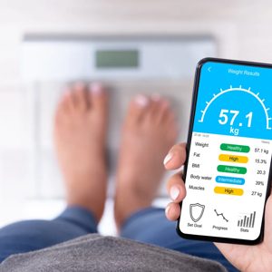 A person monitors their fitness progress while standing on a scale, showcasing a commitment to health and well-being. The mobile app provides detailed metrics such as weight and body composition, symbolizing the modern approach to personal fitness tracking.