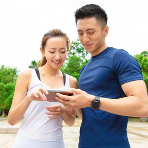 A young couple enjoys quality time outdoors, sharing a moment of laughter as they explore an app on their smartphone, surrounded by lush green trees and a scenic park setting.