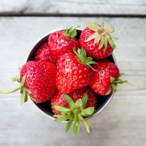 A bountiful harvest of fresh strawberries fills a rustic metal bowl, showcasing their vibrant red hue and green leafy tops, inviting you to enjoy their sweet, juicy flavor. Perfect for summer desserts or a healthy snack!