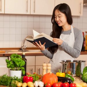 In a cozy kitchen, a young woman prepares to create a culinary masterpiece, pouring over recipes as fresh ingredients surround her, each chosen with care for a delicious meal ahead.