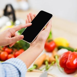 In a vibrant kitchen filled with fresh produce, a person interacts with their smartphone, blending technology and culinary creativity. The colorful assortment of vegetables and fruits inspires healthy cooking and meal planning.