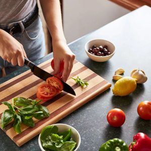 In a vibrant kitchen filled with fresh ingredients, a skilled cook deftly slices ripe tomatoes on a classic wooden cutting board, preparing for a delicious meal that showcases the beauty of culinary art and healthy eating.