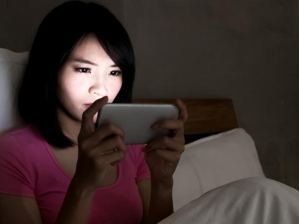 Woman using phone in bed at night