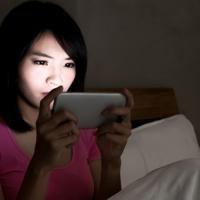 Woman using phone in bed at night