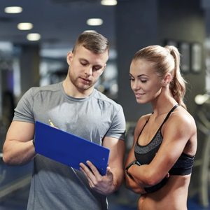 In the heart of a bustling gym, a dedicated trainer reviews workout plans with a motivated athlete, both focused on achieving their fitness goals together.