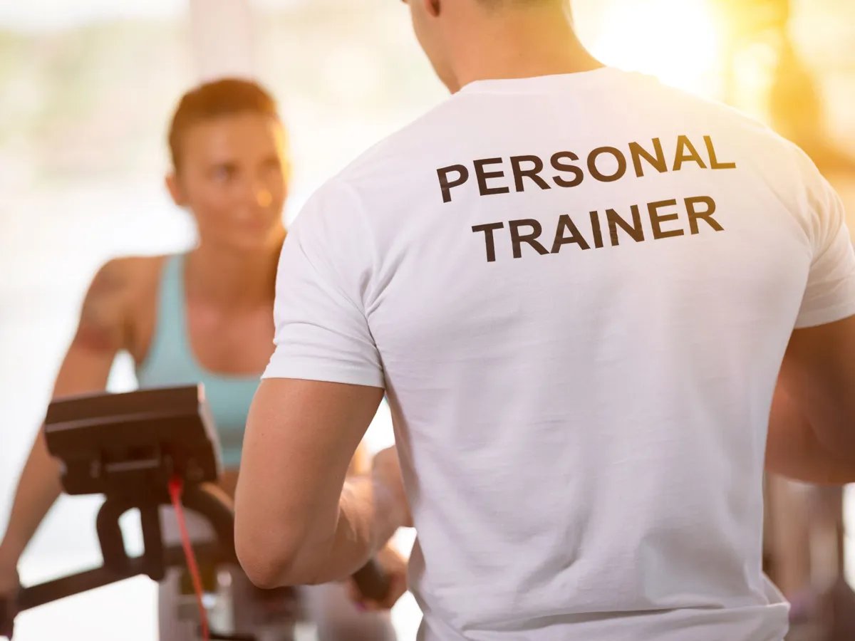 In a vibrant fitness studio, a dedicated personal trainer motivates a client on a stationary bike, embodying the spirit of personal wellness and empowerment. Their shared focus on fitness underlines the importance of guidance in achieving health goals.