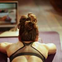 Stretches on a yoga mat while watching virtual fitness class